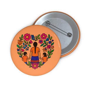 May include: A round, orange button with a floral heart design. The heart frames a mother figure holding hands with two children. The design features colorful flowers in pink, blue, and orange. A second button is partially visible.