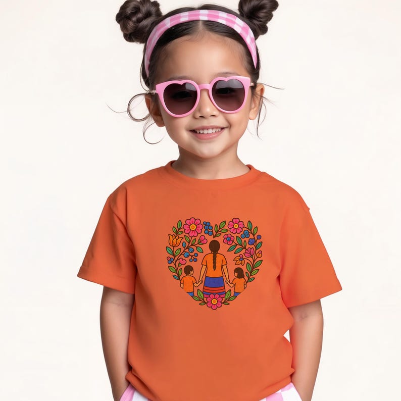 May include: An orange t-shirt featuring a heart-shaped floral design with a mother and two children. The design includes pink, blue, and orange flowers. The child in the image is wearing pink heart-shaped sunglasses and a pink and white checkered headband.