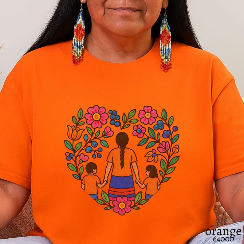 May include: Orange t-shirt featuring a heart-shaped floral design with a mother and two children holding hands. The design includes pink and blue flowers, green leaves, and a brown-haired mother figure. The text "orange 64000" is printed at the bottom right.