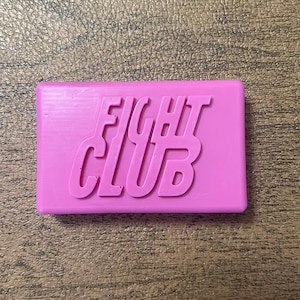 Puede incluir: Una pastilla de jabón rectangular de color rosa con las palabras "FIGHT CLUB" en relieve en la parte delantera.