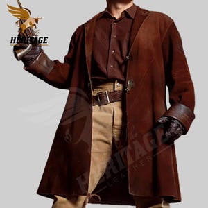 Puede incluir: Un abrigo largo de gamuza marrón con un cinturón de cuero marrón y guantes de cuero marrón. El abrigo tiene cierre de botón y cuello.