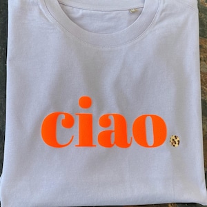 Op de afbeelding: Een lavendelkleurig T-shirt met het woord "ciao" in oranje gedrukt.