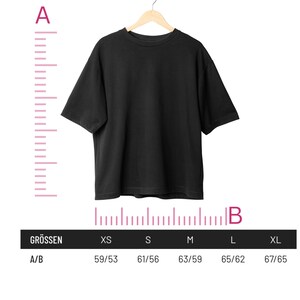 Op de afbeelding: Een zwart T-shirt hangt aan een houten hanger. Een maattabel toont de afmetingen in centimeters voor de maten XS, S, M, L en XL. De tabel is ge&euml;tiketteerd met "Gr&ouml;ssen" en "A/B".