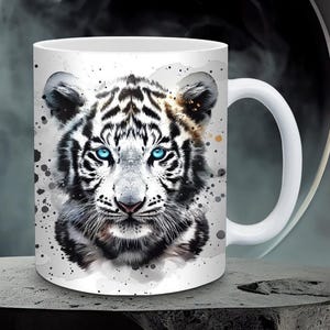 May include: White ceramic mug with a watercolor-style image of a white tiger with blue eyes. The tiger's face is centered on the mug and fills most of the space.