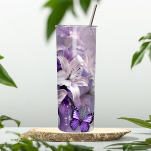 Puede incluir: Un vaso de acero inoxidable con un dise&ntilde;o floral morado y blanco con lirios y una mariposa morada. El vaso tiene una tapa y una pajita.