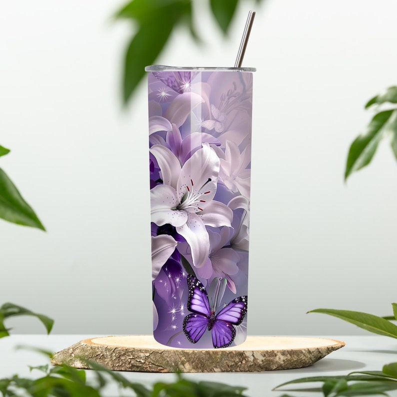 Puede incluir: Un vaso de acero inoxidable con un dise&ntilde;o floral morado y blanco con lirios y una mariposa morada. El vaso tiene una tapa y una pajita.