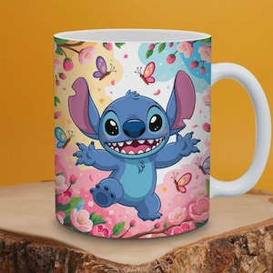 Puede incluir: Taza de cerámica blanca con un personaje de dibujos animados de piel azul, orejas grandes y una amplia sonrisa. La taza está decorada con flores rosas, mariposas y un fondo colorido. El asa es blanca.