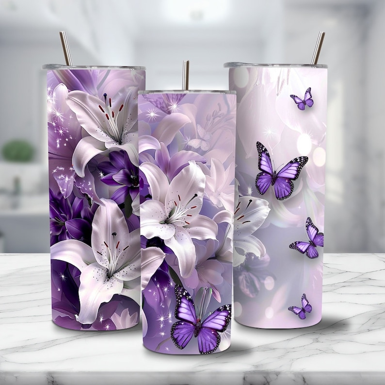 Puede incluir: Tres vasos de acero inoxidable con un dise&ntilde;o floral morado y blanco con lirios y mariposas. Los vasos tienen un acabado met&aacute;lico brillante.