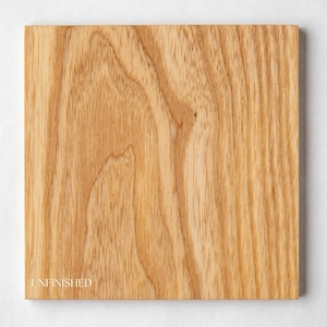 May include: A square, unfinished piece of light-colored wood with visible grain patterns. The word "UNFINISHED" is printed in a small, white font on the lower left corner. The wood has a natural, warm tone.