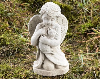May include: A white concrete angel statue with wings holding a small cat in its arms. The statue is sitting on a bed of green moss.