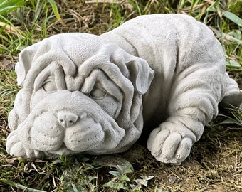 May include: A gray concrete garden statue of a Shar-Pei puppy lying down with its head resting on its paws.