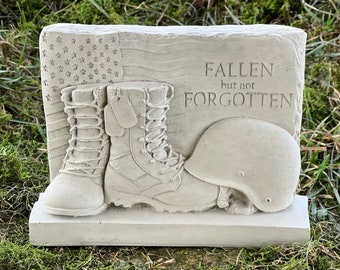 May include: A white concrete memorial with a pair of boots, a helmet, and an American flag. The text "Fallen but not Forgotten" is inscribed on the memorial.