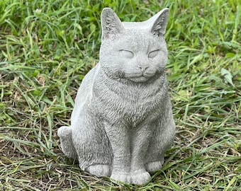 May include: A gray concrete cat statue with a realistic fur texture. The cat is sitting with its eyes closed and its head tilted slightly down.