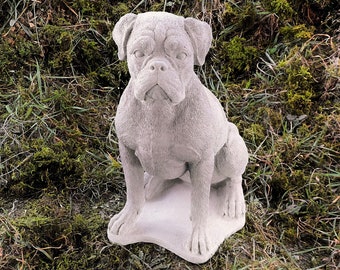 May include: A white concrete statue of a boxer dog sitting on a base. The dog is looking directly at the camera.