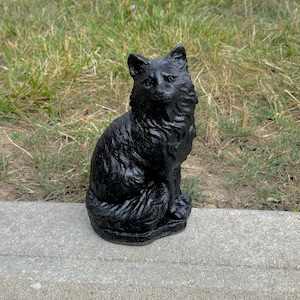 Peut inclure: Une figurine de chat noir, assise avec sa queue enroul&eacute;e autour de ses pattes. La figurine est faite d'un mat&eacute;riau lisse et fonc&eacute; et a une apparence r&eacute;aliste.
