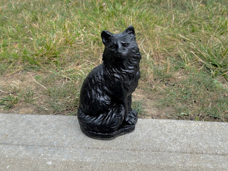 Peut inclure: Une figurine de chat noir, assise avec sa queue enroul&eacute;e autour de ses pattes. La figurine est faite d'un mat&eacute;riau lisse et fonc&eacute; et a une apparence r&eacute;aliste.