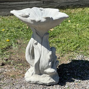 K&ouml;nnte beinhalten: Ein graues Vogelbad aus Beton in Form einer Blume mit einer breiten, flachen Schale und einem hohen, schlanken Sockel.