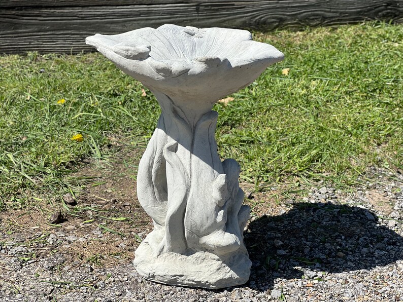 K&ouml;nnte beinhalten: Ein graues Vogelbad aus Beton in Form einer Blume mit einer breiten, flachen Schale und einem hohen, schlanken Sockel.