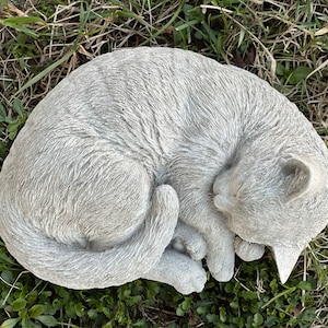 May include: A gray concrete garden statue of a cat curled up sleeping. The cat has a detailed fur texture and a realistic sleeping pose.