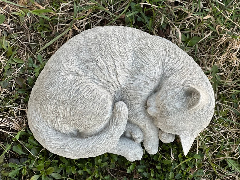 May include: A gray concrete garden statue of a cat curled up sleeping. The cat has a detailed fur texture and a realistic sleeping pose.