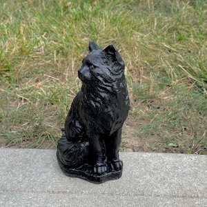 Peut inclure: Une statue de chat noir, assise avec sa queue enroul&eacute;e autour de ses pattes. La statue est faite d'un mat&eacute;riau lisse et fonc&eacute; et a une apparence r&eacute;aliste.