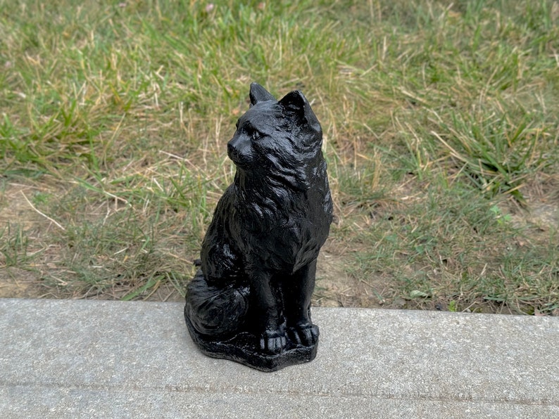 Peut inclure: Une statue de chat noir, assise avec sa queue enroul&eacute;e autour de ses pattes. La statue est faite d'un mat&eacute;riau lisse et fonc&eacute; et a une apparence r&eacute;aliste.