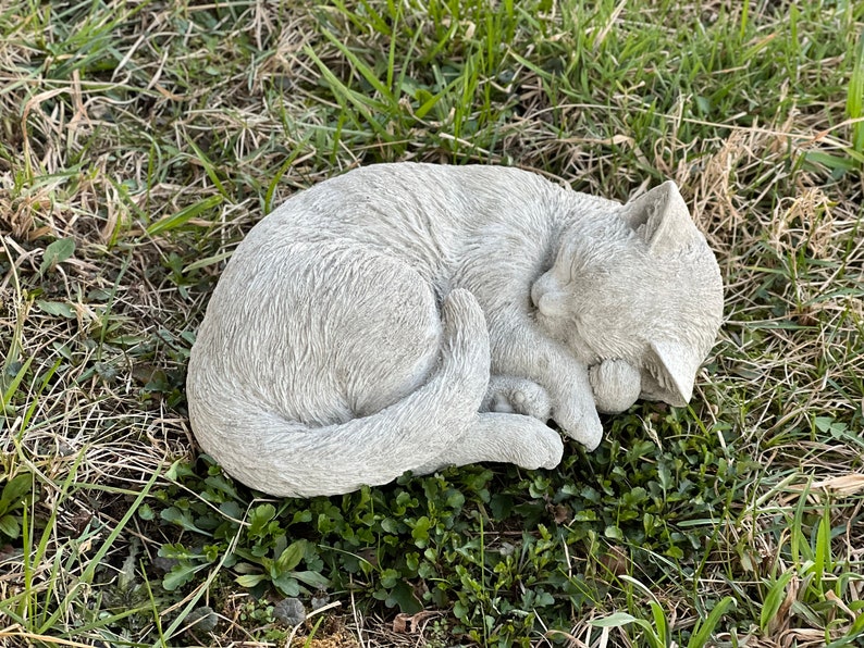May include: A gray concrete sculpture of a cat curled up sleeping. The sculpture is detailed with fur and has a realistic appearance.