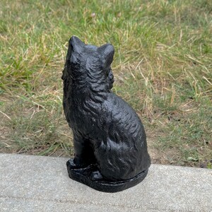 Peut inclure: Statuette de chat noir assise sur une surface en b&eacute;ton gris. Le chat est tourn&eacute; dos &agrave; la cam&eacute;ra et a une surface textur&eacute;e d&eacute;taill&eacute;e.