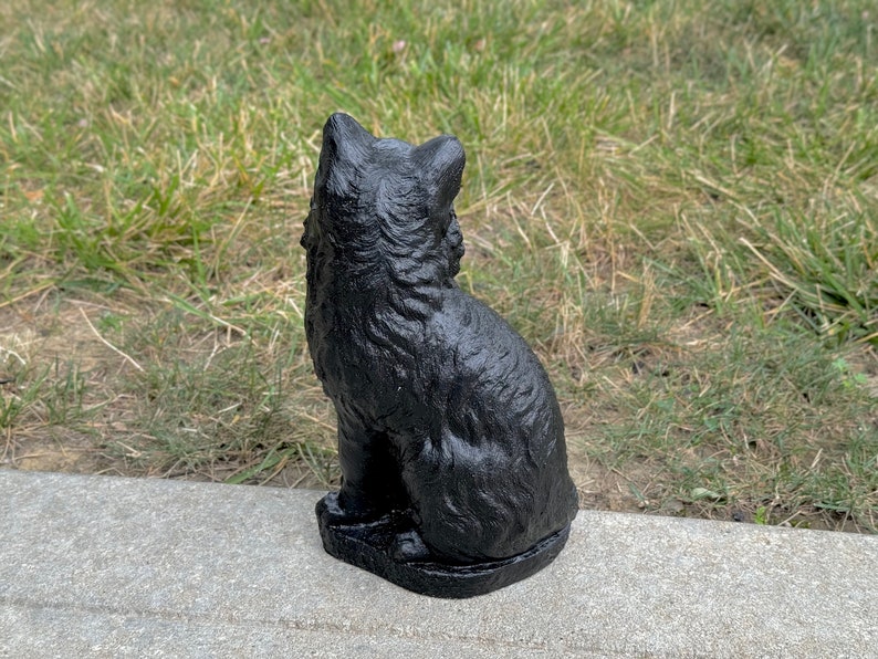 Peut inclure: Statuette de chat noir assise sur une surface en b&eacute;ton gris. Le chat est tourn&eacute; dos &agrave; la cam&eacute;ra et a une surface textur&eacute;e d&eacute;taill&eacute;e.