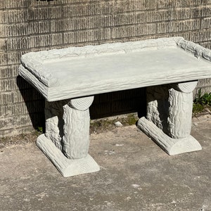 May include: A gray concrete bench with a log design. The bench has a flat top and two legs on each side. The legs are shaped like logs with bark details.