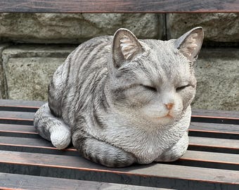 May include: A gray and white sleeping cat figurine. The cat is curled up with its eyes closed. The figurine is made of a realistic material and has a detailed texture.