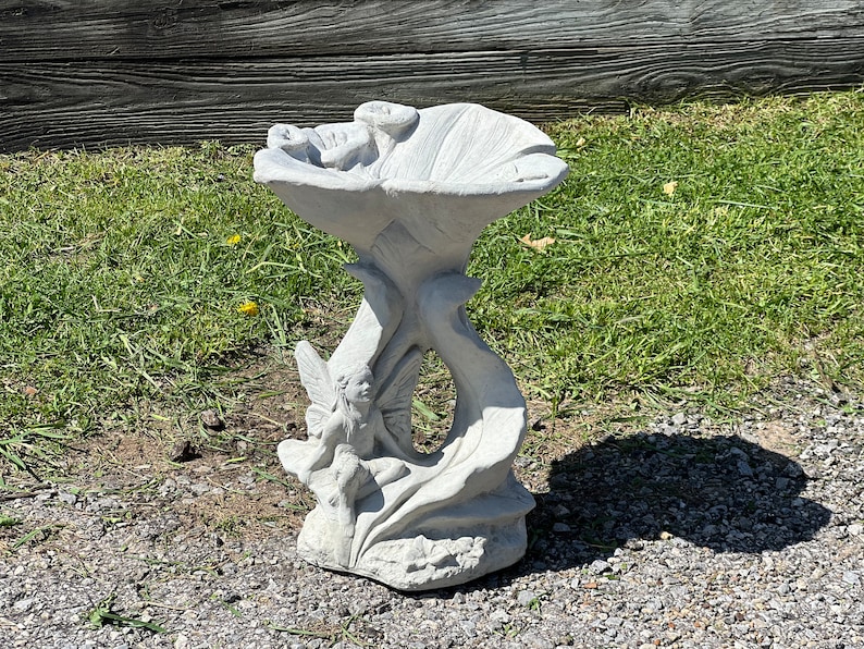 K&ouml;nnte beinhalten: Ein wei&szlig;er Vogelbad aus Beton mit einer Feenskulptur auf der Basis. Das Vogelbad ist blumenf&ouml;rmig mit einer breiten, flachen Schale.