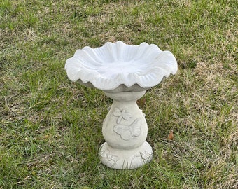May include: A white concrete bird bath with a scalloped edge and a base decorated with butterfly designs.