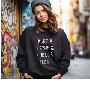 以下が含まれることがあります： 白い文字で「Kurt & Layne & Chris & Eddie.」と書かれた黒いスウェットシャツ