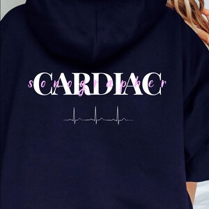 May include: A navy blue hoodie with a white graphic that says "Cardiac Sonographer" with a pink EKG line underneath.