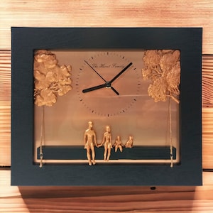 May include: A rectangular clock with a dark blue frame. The clock face features a family silhouette and the text "The Hurst Family." Gold-colored trees and family figures are on the clock face.