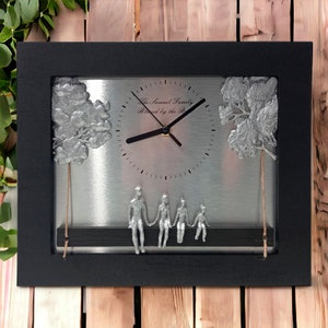 May include: A black framed clock with a silver face and a family of five figures sitting on a bench. The clock face has the text "The Samuel Family Blessed by the Lord" and a silver tree on each side.