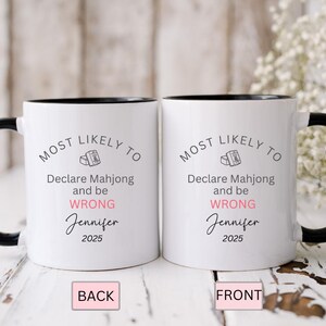 May include: Two white ceramic mugs with black handles and rims. The mugs have the text "MOST LIKELY TO Declare Mahjong and be WRONG Jennifer 2025" printed on them. The word "WRONG" is in pink.