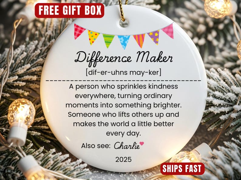 以下が含まれることがあります： 「Difference Maker」の文字と定義が書かれた白いセラミック製のクリスマスオーナメント。カラフルなバナーと「Also see: Charlie」の文字、2025年が装飾されています。