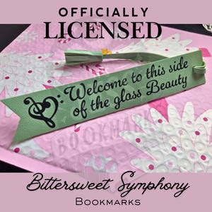 Peut inclure: Un marque-page vert avec le texte "Welcome to this side of the glass Beauty" et un motif de note de musique. Le marque-page a une gland et est étiqueté "Bittersweet Symphony Bookmarks."
