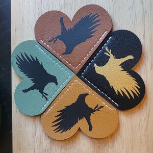 May include: Four heart-shaped leather bookmarks with different colored backgrounds and black silhouettes of birds. The bookmarks are sewn together to form a clover shape.