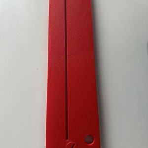 May include: A red plastic tool with a long, thin slot and a small hole. The tool is designed for use with a specific type of hardware.