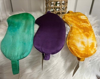 May include: Three sleep masks in different colors and patterns. The first mask is green with a tie-dye pattern. The second mask is purple with a satin finish. The third mask is yellow with a tie-dye pattern.