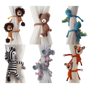 Puede incluir: Colección de seis sujetacortinas de ganchillo con forma de animales. Los sujetacortinas incluyen leones, un oso, dinosaurios, una cebra, elefantes y tigres. Cada animal es de un color y diseño diferente, con los elefantes usando tutús rosas.
