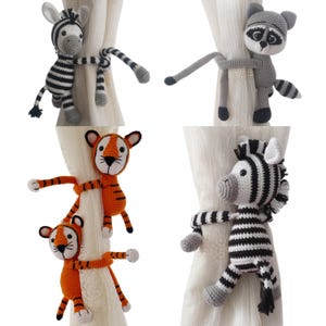 May include: Five crocheted animal curtain tiebacks. The tiebacks are in the shape of a zebra, a raccoon, a tiger, and two zebras. The tiebacks are all in different colours and patterns.