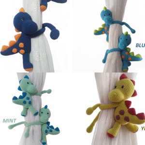 May include: Set of four crocheted dinosaur curtain tie backs in navy blue, blue, mint green, and yellow. Each dinosaur has orange spots and a curled tail.