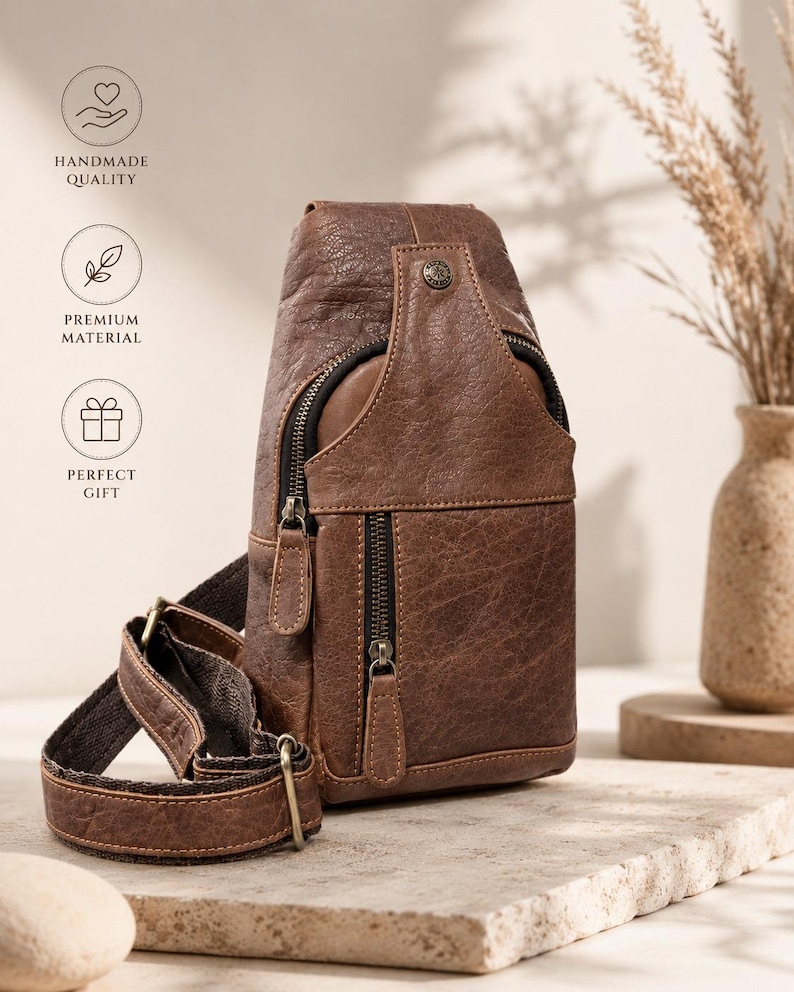 May include: A brown textured leather sling bag featuring a vertical zippered front pocket, a main zippered compartment, and an adjustable strap with metal hardware. The bag includes a small circular metal stud detail near the top closure.