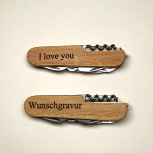 Puede incluir: Dos navajas de bolsillo de madera con múltiples herramientas. La navaja superior tiene grabado "I love you" en el mango de madera. La navaja inferior tiene grabado "Wunschgravur". Ambas navajas tienen un sacacorchos.