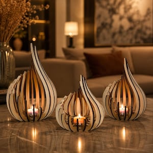 May include: Three flame-shaped candle holders constructed from layered light-coloured wood with dark edges. Each holder features a curved, open-slatted design that tapers to a point at the top, with a small lit tea light candle placed inside each base.