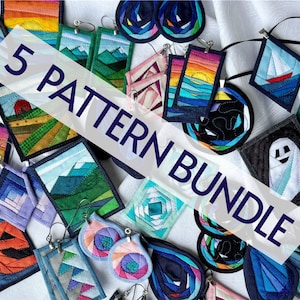 May include: A collection of fabric earrings featuring diverse geometric and landscape designs, including mountains, sunsets, a sailboat, and a ghost. The pieces are stitched with colorful fabric strips and include metal earring hooks and findings.